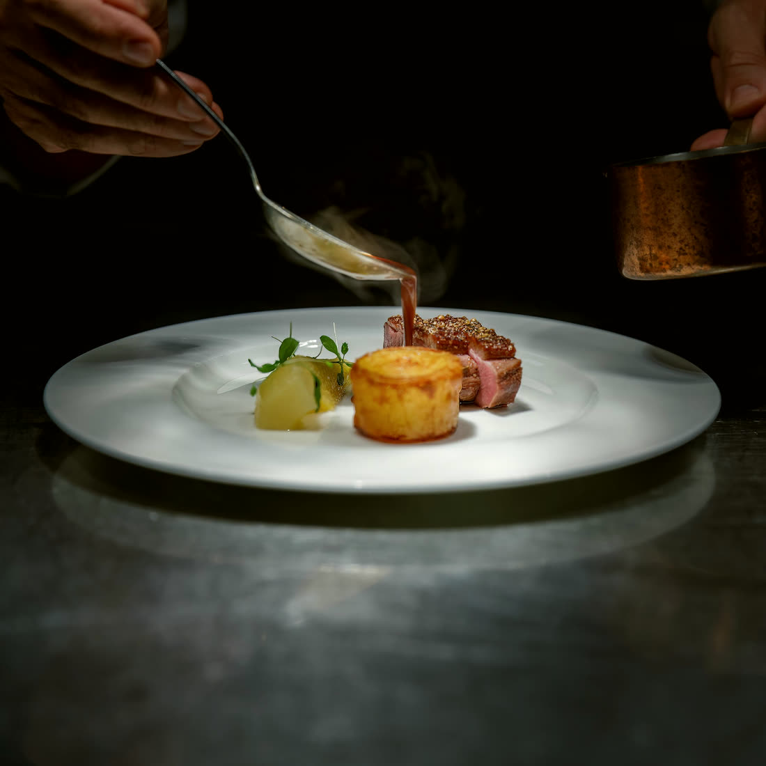 A chef spooning sauce over a plated steak