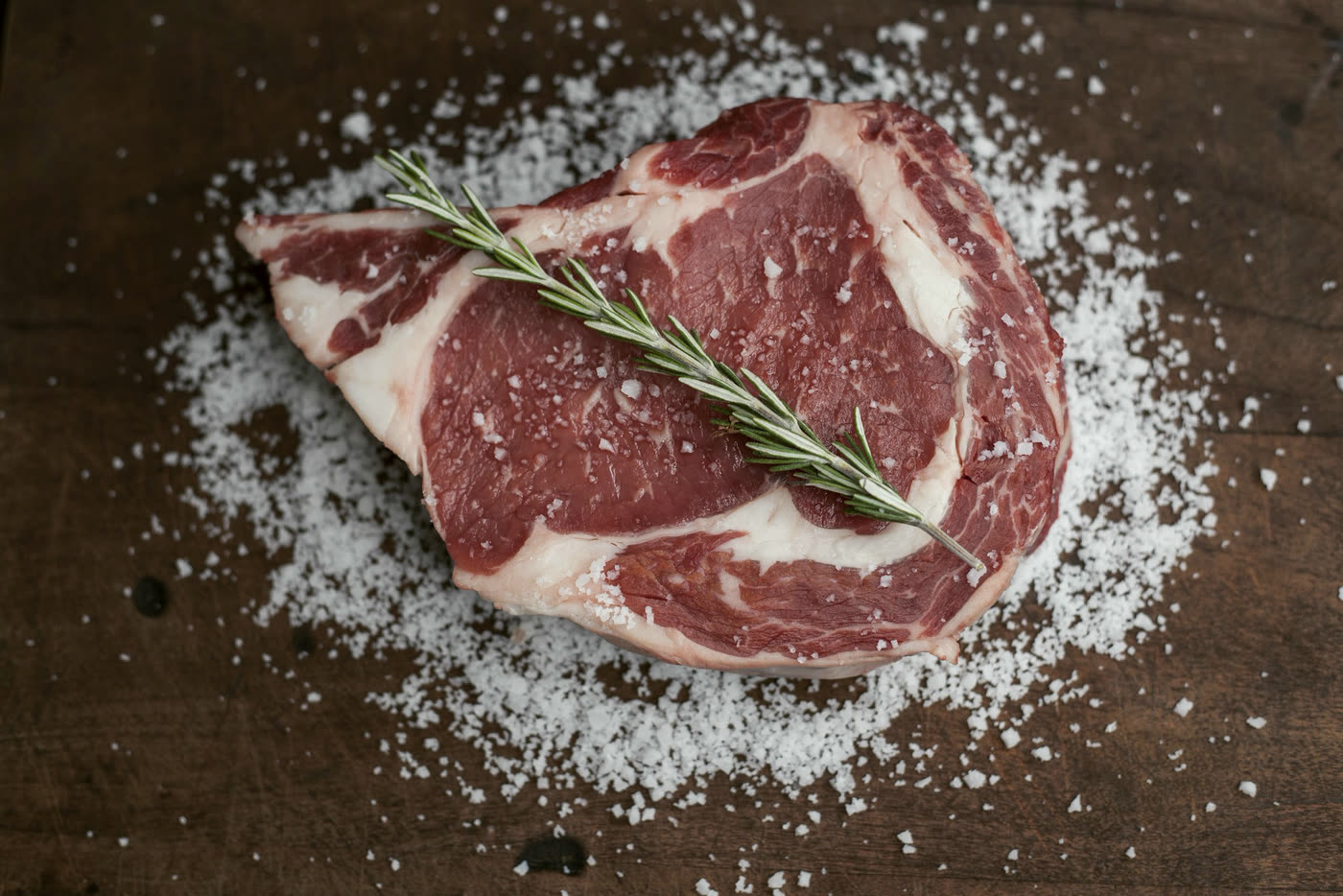 A raw ribeye resting on coarse salt on an oak board